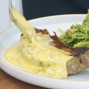 Grilled steak topped with creamy yellow cheese sauce, served with a side of green salad on a white plate.